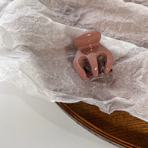 Detail of a small dusty rose resin hair claw clip on a wooden tray with a minimalist aesthetic