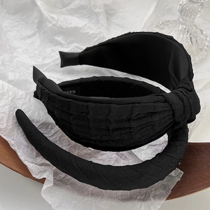 Detail of black textured fabric headband featuring a top knot design and handmade label
