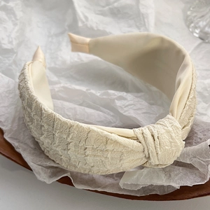 Detailed view of beige pleated fabric headband with top knot on a wooden tray