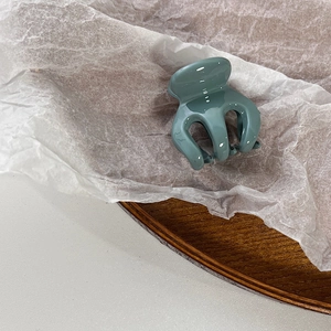 Detail view of a small greyish blue glossy hair claw clip on soft white decorative paper