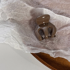 Detail view of a small brown plastic hair claw clip with a glossy finish on white paper