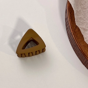 Vue détaillée d'une pince à cheveux triangulaire marron mat sur une surface blanche
