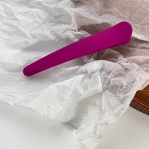 Macro shot of matte magenta candy-colored hair clip on white textured paper
