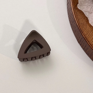 Détail d'une pince à cheveux triangulaire marron mat avec design évidé sur fond blanc