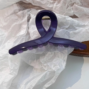 Détail d'une pince à cheveux violet foncé effet gelée avec ressort métallique sur bois