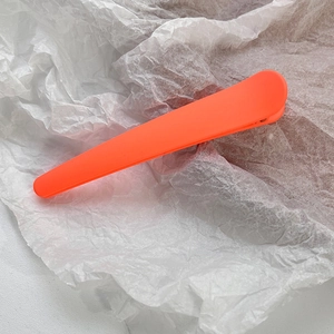 Detail shot of a matte neon orange rectangular hair clip on a white textured background