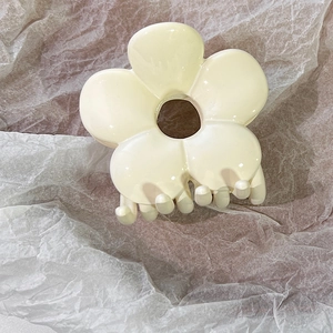 Close-up of cream white resin flower hair claw clip on soft grey textured paper