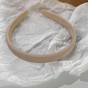 Détail du serre-tête en tissu beige avec texture fine sur fond de papier de soie blanc