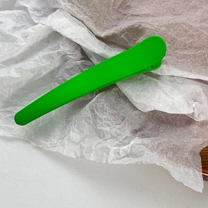 Close-up of bright green matte finish hair clip with long beak design on white paper
