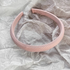 Détail d'un serre-tête en tissu sergé rose clair avec une texture plissée sur fond blanc