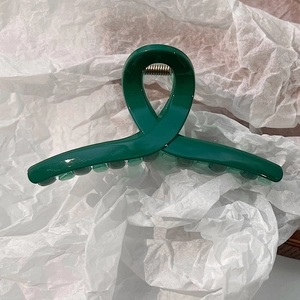 Détail d'une pince à cheveux vert foncé en résine au design croisé sur papier texturé blanc