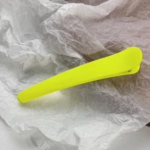 Macro shot of a neon yellow matte hair clip on a textured white background paper