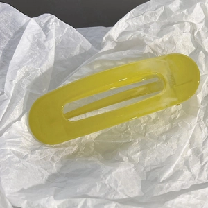 Gros plan d'une pince à cheveux ovale jaune translucide sur fond de papier froissé