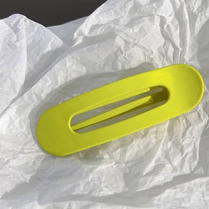 Pince à cheveux évidée jaune néon minimaliste sur papier de soie blanc texturé