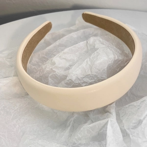 Detailed top view of a cream padded faux leather headband on a textured paper background
