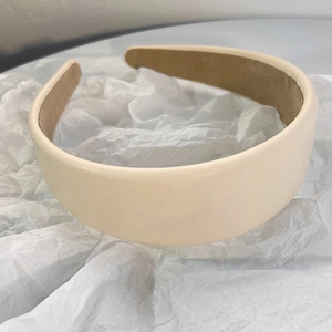 Detail of a creamy beige padded headband in faux lambskin leather on a white paper background