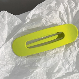 Gros plan d'une pince à cheveux rectangulaire vert fluo mat sur fond blanc texturé
