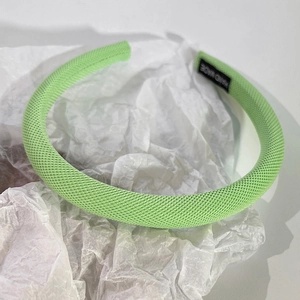 Détail d'un serre-tête éponge vert clair avec étiquette faite main sur papier blanc
