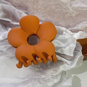 Detailansicht der großen orangefarbenen matten Blumen-Haarklammer auf weichem Papier
