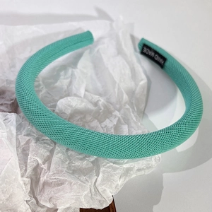 Détail d'un serre-tête vert menthe avec étiquette Hand Made tissée et texture en tricot