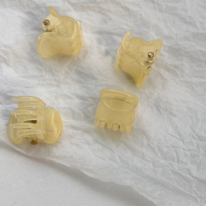 Detail view of four cream-colored mini hair clips arranged on a soft white background