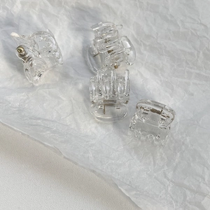 Detail view of four mini clear hair claws made of transparent plastic with metal springs