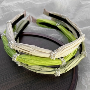 Detailed view of pleated satin headbands with white pearls on a rustic wooden tray