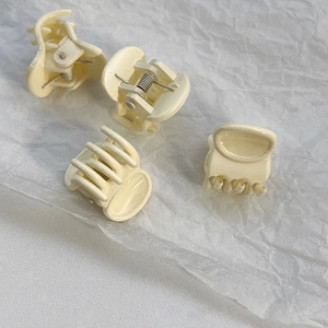 Detailed view of four mini cream-colored hair claw clips set on white textured paper