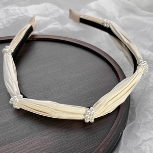 Detail of cream pleated satin headband with small pearl clusters on a wooden tray