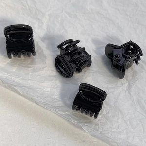 Detailed macro view of four mini black plastic hair clips with metal springs