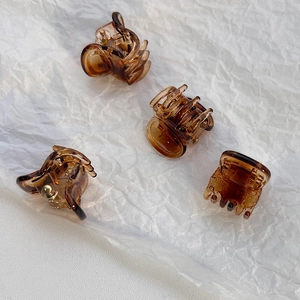 Macro detail of four amber resin mini hair claws with strong metal springs on white paper