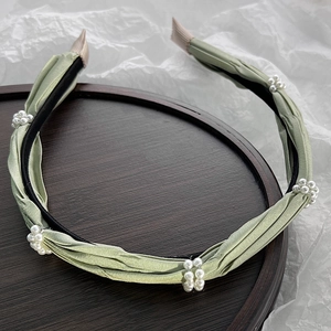 Detail of light green satin headband with pearl clusters on a wooden tray background
