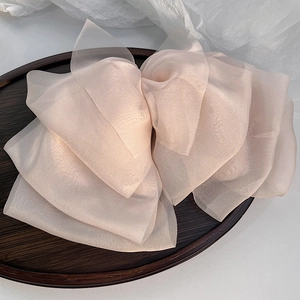 Detail of the layered oversized chiffon bow hair clip in soft apricot pink on a wooden tray