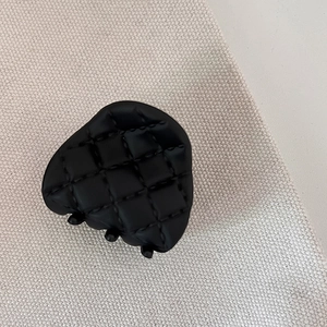 Detail of matte black heart-shaped hair claw with classic quilted grid pattern texture