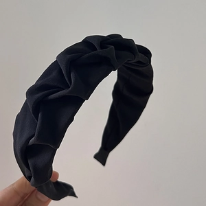 Close-up of black pleated twist headband showing matte fabric texture and wide frame detail