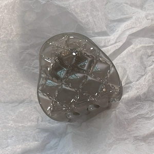 Détail d'une pince à cheveux grise translucide avec texture matelassée et motif de grille
