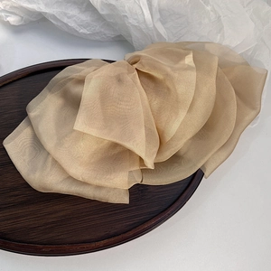 Detailed macro shot of elegant champagne gold layered chiffon bow hair clip on wooden tray