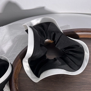 Detail of elegant black and white pleated satin hair scrunchie in a wooden tray