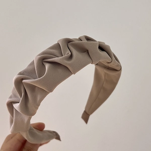 Close-up detail of beige pleated fabric headband showing fine texture and wavy retro style