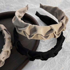 Close-up of pleated fabric headbands in beige and black colors on a wooden tray