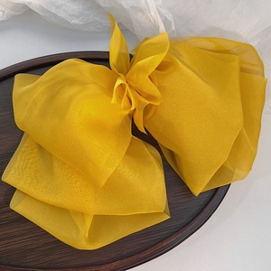 Macro shot of large bright yellow layered chiffon bow hair clip on a wooden tray