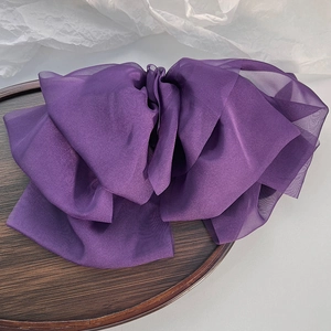 Detailed view of a multi-layer purple chiffon bow hair clip on a wooden display tray