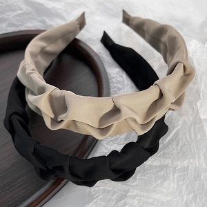 Detailed texture of pleated fabric headbands in black and beige on wooden tray