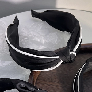Detail of elegant black satin headband with white piping and central knot design