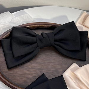 Dettaglio di un grande fiocco per capelli in raso nero su un vassoio di legno vintage