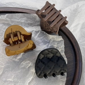 Detail view of three matte quilted hair claws in dark brown, yellow, and black colors