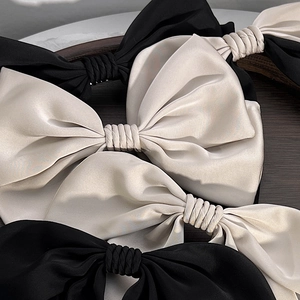 Elegant large satin bow hair clip in black and off-white silk on a wooden tray