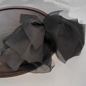 Detail of a large black multi-layer organza bow hair clip on a wooden tray