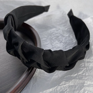 Close-up of black pleated fabric headband with twisted knot design on a wooden tray