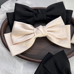 Dettaglio di eleganti fermagli per capelli con fiocco in raso nero e champagne su vassoio in legno